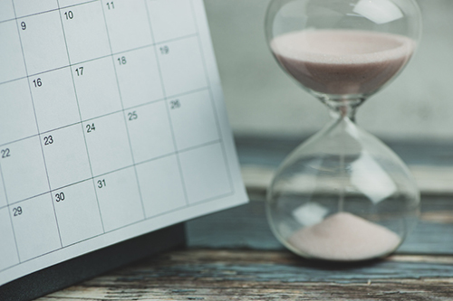 Calendar and hourglass on wood table, vintage style.